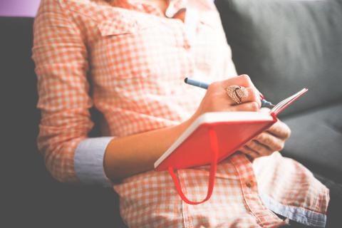 person writing in red journal