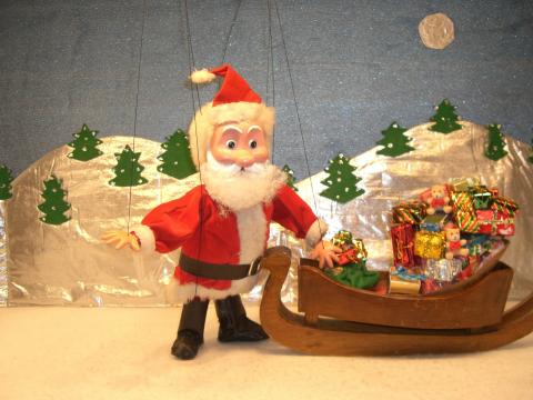 A Santa Claus marionette standing by a sled