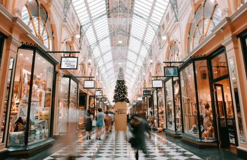 Photo of a mall of shoppers moving quickly, blurred; mall is decorated for winter holidays