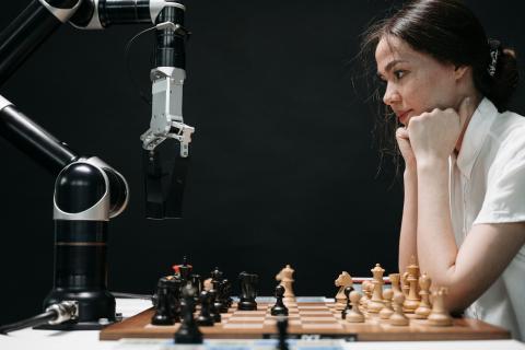 A young woman playing chess against a robot arm