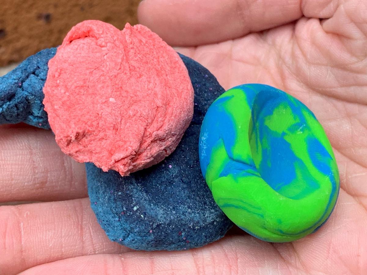 Red, green, and blue clay stones on palm of hand with red brick background. 