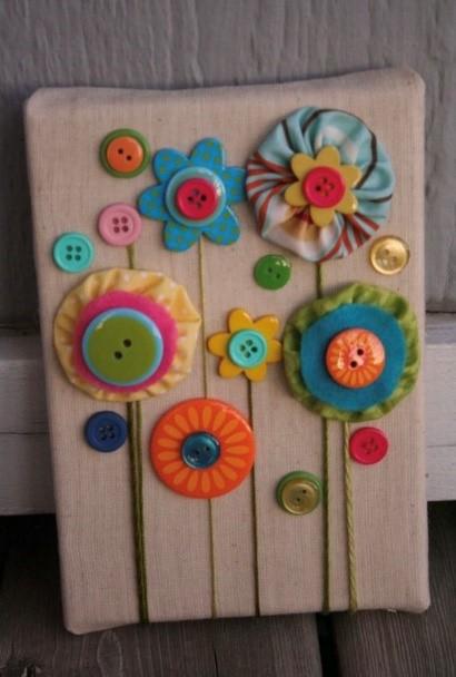 Colorful buttons, fabric, and string arranged to look like flowers on a canvas.