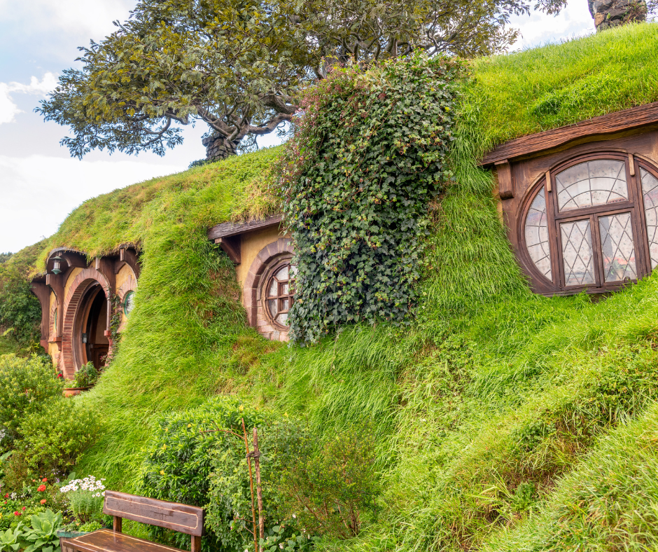 A hobbit home in the Shire, with a round door and round windows, covered in vegetation.