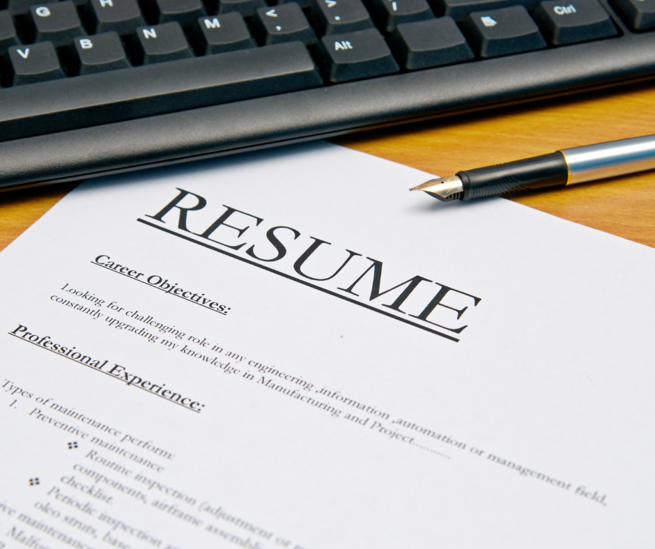 A paper resume on a desk tucked under a pen and computer keyboard.