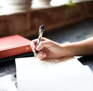 close up of a person's hand writing in a journal with a pen