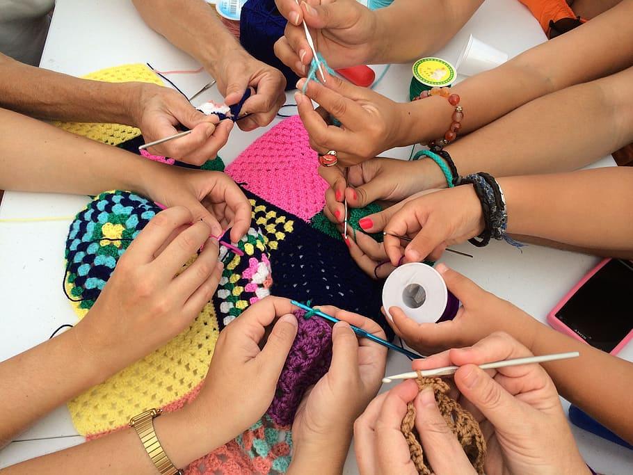 close up of several hands in a circle all in various stages of crocheting