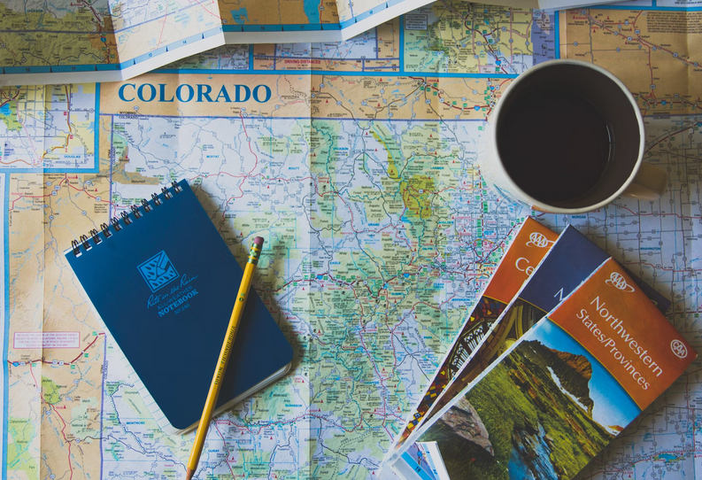 photo of a notebook, maps, and cup of coffee sitting on top of a road map