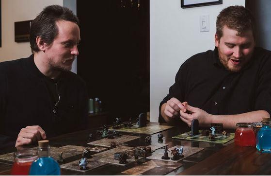 photo of two men sitting at a table with figures and dice playing Dungeons and Dragons