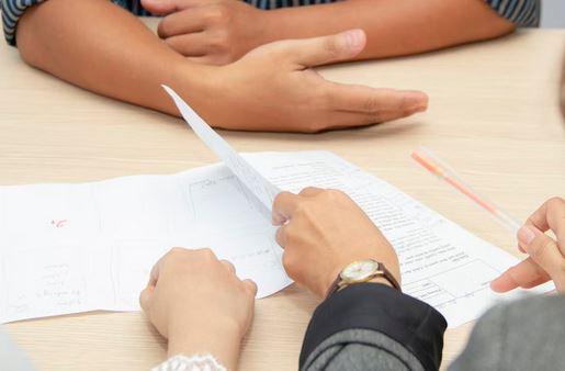 close up of hands resting on a table and another set of hands flipping through a paper resume